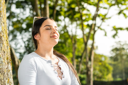 portrait of beautiful latin woman, with her eyes closed and raising her head to breathe the pure air of nature.の写真素材