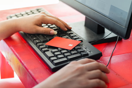 woman with her hands on the keyboard using the computer, with her credit card placed on top of the keyboardの写真素材