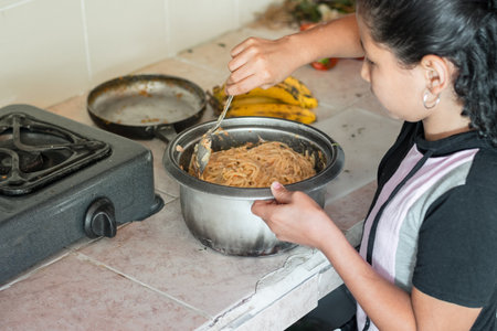 little latin brunette girl, using a spoon to stir spaghetti. learning how to cookの写真素材