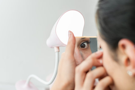 detailed view of a latina woman's eye in the mirror, while applying make-upの写真素材