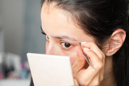 close-up of a beautiful latina teenager plucking her eyebrows with a pair of tweezersの写真素材