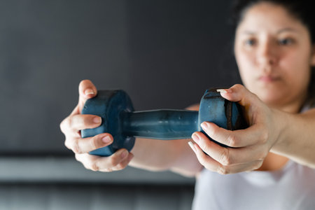 close-up of a latina girl holding a dumbbell with both hands, exercising at home.の写真素材