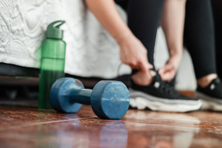detailed shot of a blue dumbbell next to a bottle of water and in the background a girl putting on her tennis shoesの写真素材
