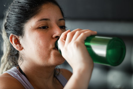 detailed view of the face of a latina woman sweating the skin of her face while drinking water from her water bottleの写真素材
