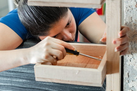 young latina woman, looking attentively at how to assemble wooden shelfの写真素材
