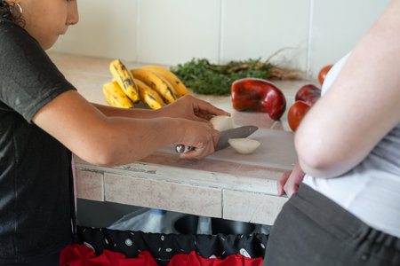 little latina girl, splitting an onion with a knife, learning to cook with her mother watchingの写真素材