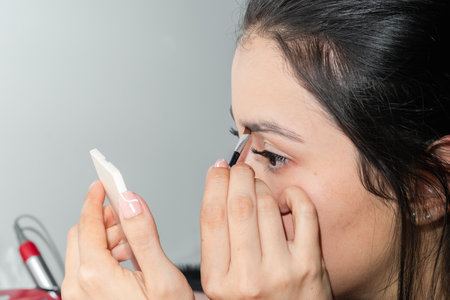 detailed view of the face of a Latin woman carefully applying makeup to her eyebrows with a small brushの写真素材