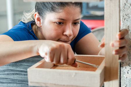 young latina woman, very focused, assembling a wooden shelf for her business.の写真素材
