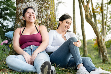 young women sitting on the ground next to a tree, talking and laughing loudlyの写真素材