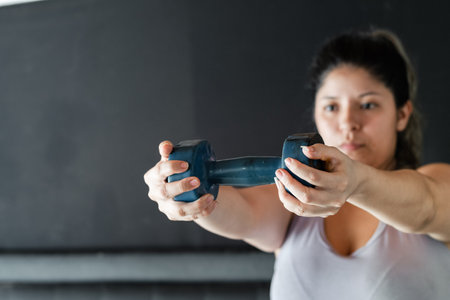 latina girl holding a dumbbell with her two hands. working out at homeの写真素材