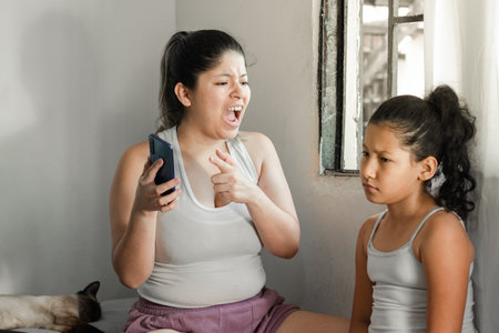 mother yelling and scolding her little daughter to put down her cell phone and go do her homework.の写真素材