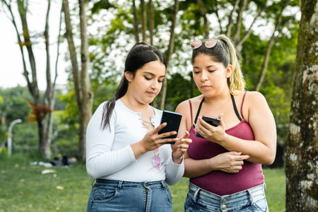 girl showing her friend the text messages she has on her cell phone while taking a walk in the park.の写真素材