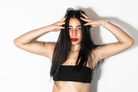 beautiful brown skinned latina woman posing frontally with both hands on her headの写真素材