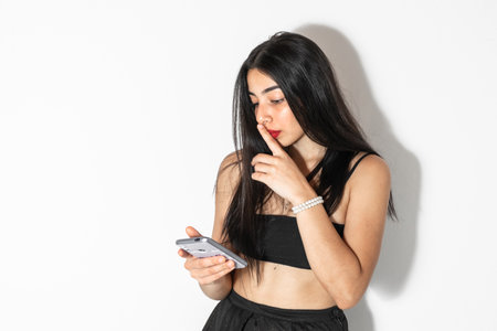 young latina woman with her cell phone in her hand and making a silent gesture while looking at her social networksの写真素材