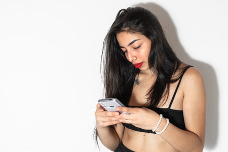 beautiful brunette latina woman, looking at her cell phone, standing against a white backgroundの写真素材