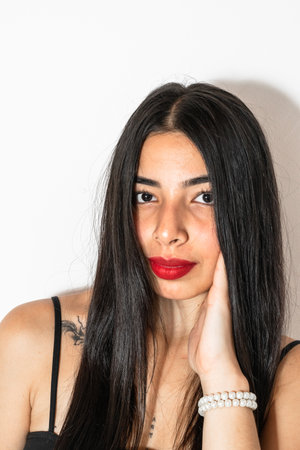 close-up portrait of a beautiful young latina woman with a hand on her cheek looking straight ahead.の写真素材