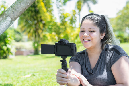 young latina woman very happy and smiling recording a vlog of her life in an outdoor parkの写真素材