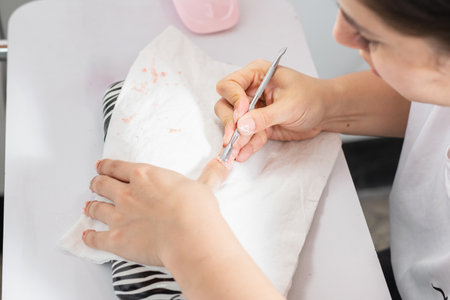 top view of a girl manicurist removing nail polish from her nails with a cuticle pusherの写真素材