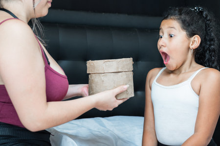 little brunette latina girl looking with great surprise at her mother who is handing her a gift.の写真素材