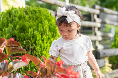 Beautiful little brunette girl, looking at and touching the red flowers in the gardenの写真素材