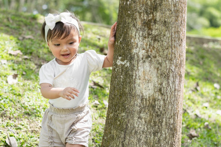 beautiful little brunette girl, playing around a large tree, surrounding it while smiling happilyの写真素材