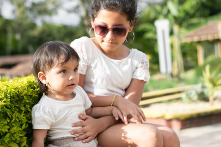 brunette latina girl taking care of her little sister while sitting in a parkの写真素材