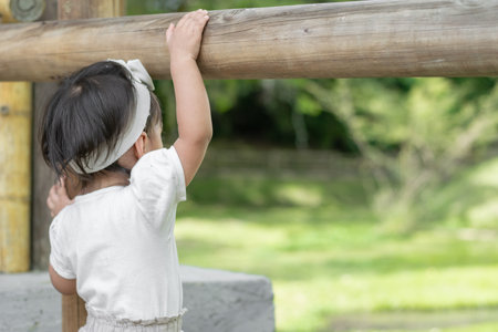 view of the back of a little latin girl standing next to the wooden fence admiring natureの写真素材