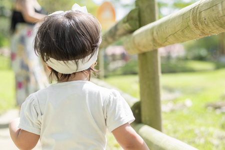 view of the back of a little latin girl walking along a nature trail next to a wooden fence.の写真素材