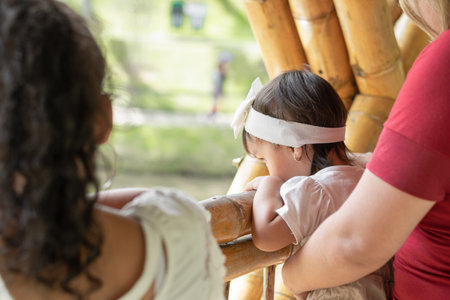 close-up of a little brown girl being carried by her mother with her sister next to her leaning against the bamboo fenceの写真素材