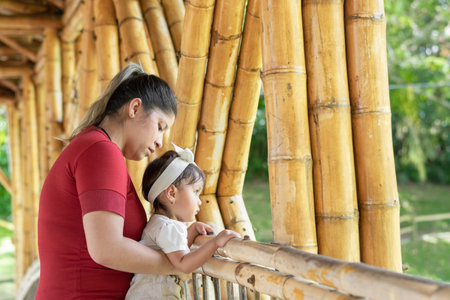 latina mother carrying her young daughter walking across a bamboo bridge while enjoying the sceneryの写真素材