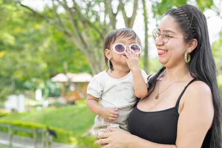 latina mother holding her smiling baby daughter, while the baby puts on her glasses.の写真素材
