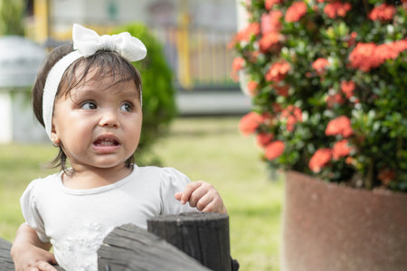 Little brunette girl with a look of surprise and disgust, looking upwards, standing next to a black wooden fenceの写真素材