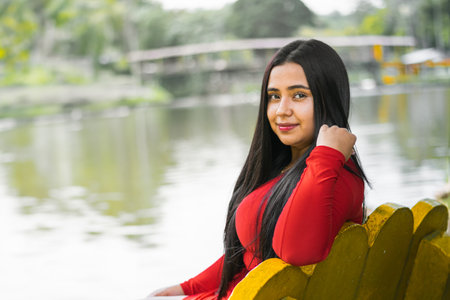 young college student sitting on a yellow chair by a lake, looking to the sideの写真素材