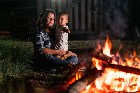 young latin woman carrying her child, sitting in front of a campfire at night, curious child pointing toの写真素材