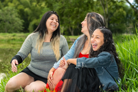 Latina friends sitting on the lawn while laughing loudly and hanging out with each otherの写真素材