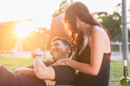 young latin couple sitting on the grass smiling and playing while she tickles him.の写真素材