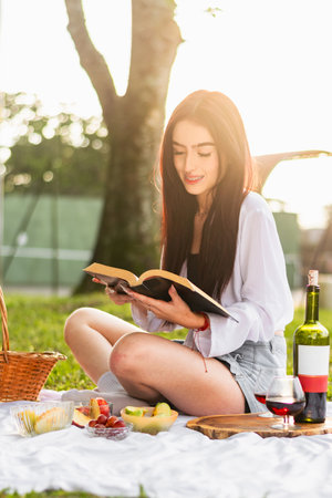 very happy and smiling slim latin girl reading a book with a golden sunset in the backgroundの写真素材