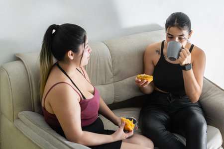 young woman drinking coffee with her friend while having a snackの写真素材