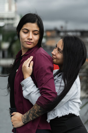 young latina lesbian couple, woman hugging her partner from behind while looking into each other's eyesの写真素材