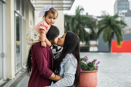 young couple kissing each other while one of them holds her daughter on her shoulders, girl looking...