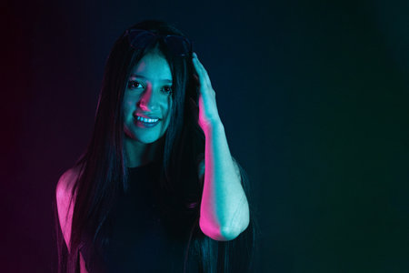 young Latina woman smiling while placing a hand on her head, posing in studio light.の写真素材