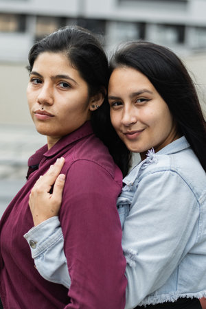 close-up of a young latina lesbian couple, woman hugging her girlfriend from behind while looking at the cameraの写真素材