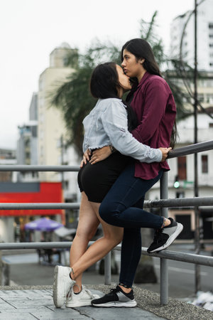 couple of lesbian women hugging and giving love to each other next to a railing in the street, college womenの写真素材