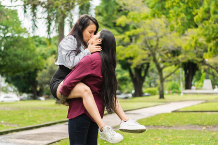 young latin lesbian couple kissing in a public park, one holding the other in her arms and holding her face, passionate kiss.の写真素材