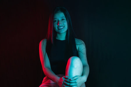 young latina woman smiling as she sits holding her calf, illuminated by studio lights.の写真素材