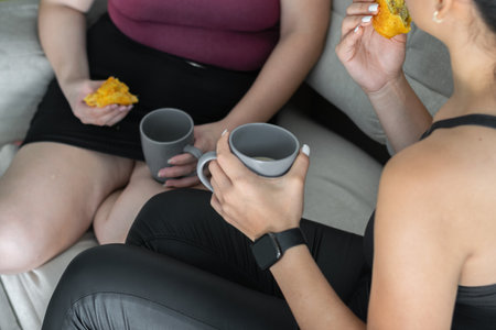 close-up of the hand of a young woman holding a cup of coffee while talking to her friend, sitting...