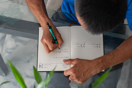 Overhead view of hands filling planner on glass table, daily planningの写真素材