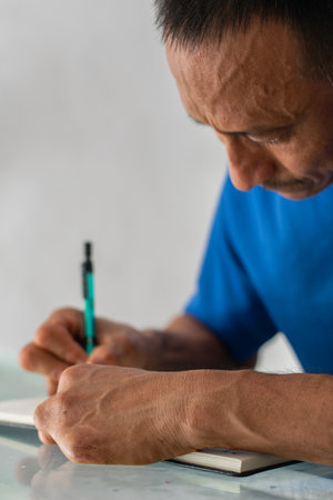 Tight portrait showing man writing with pen, face and left hand visible, four left fingers amputatedの写真素材