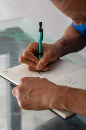 Close crop of hands and pen writing in planner, clear view of left hand missing four fingers, detailed shotの写真素材