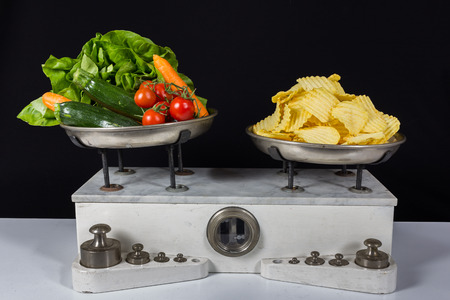 Balance with two metal plates with weights, vegetable and chipsの写真素材
